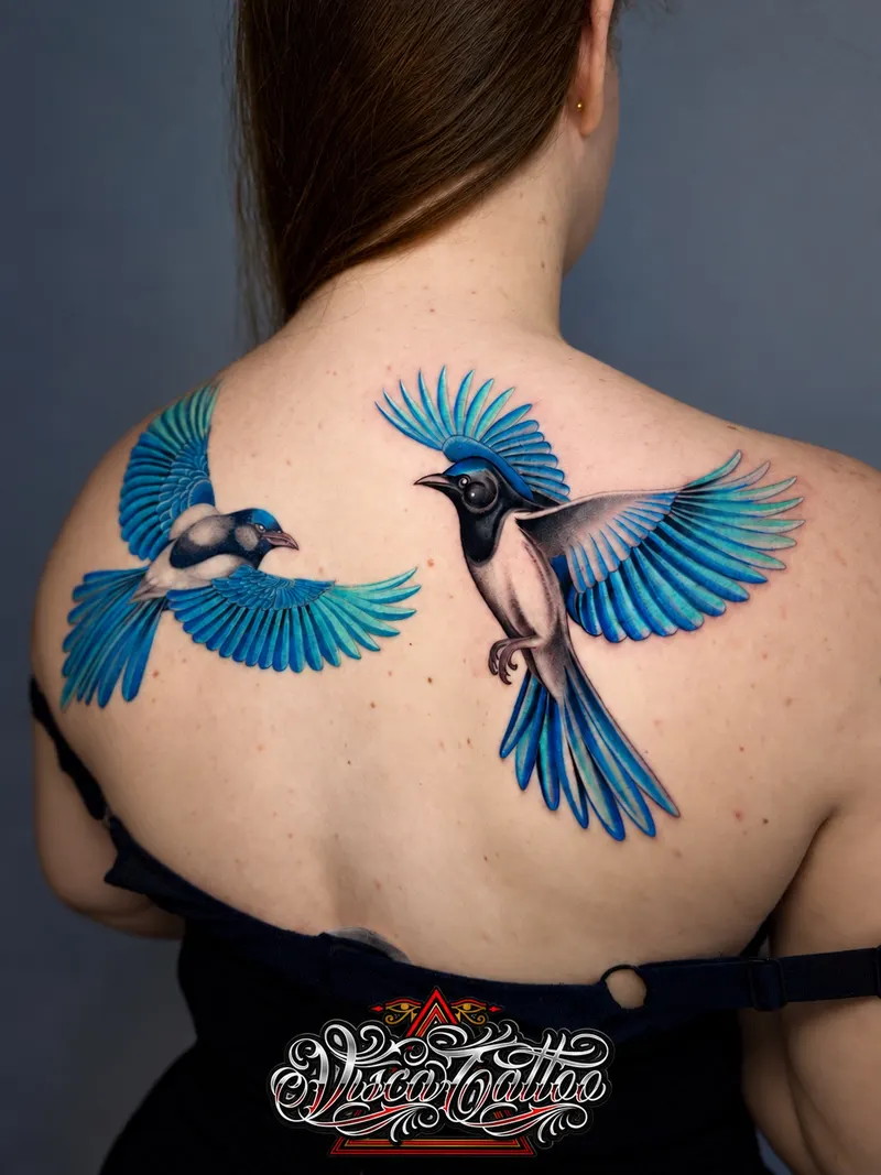Two blue birds in flight tattooed across a back